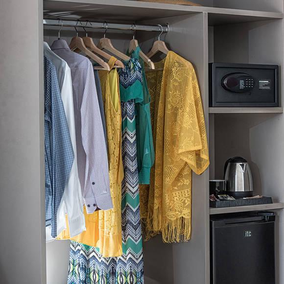 Open wardrobe featuring clothes, a safe, kettle, mugs, and a mini fridge