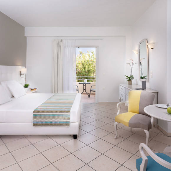 Double room with white furnishing, cozy seating area, wall-mounted TV and balcony view of greenery