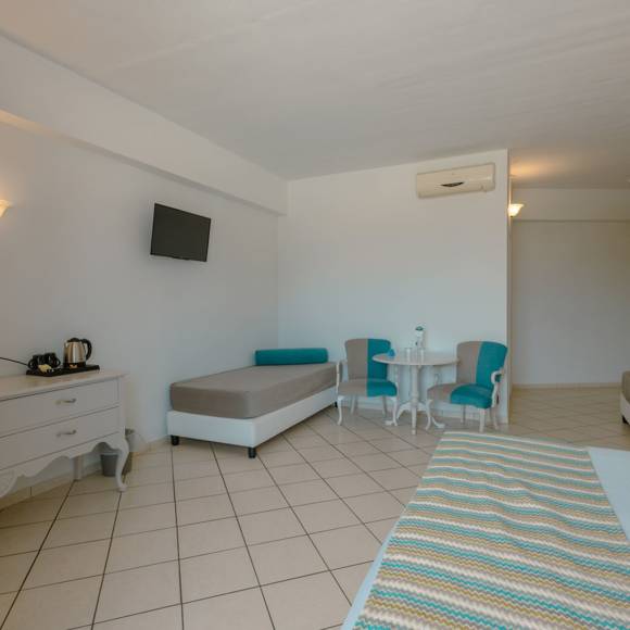 Quadruple room interior with two single beds, vanity desk, armchairs and a wall-mounted TV