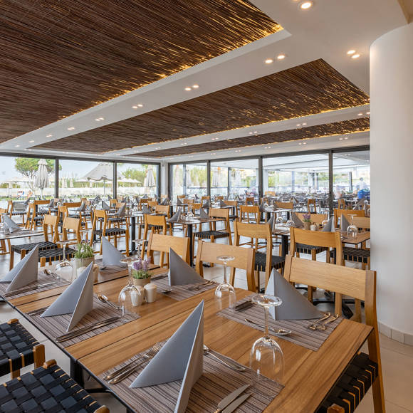 Modern restaurant with wooden chairs and tables, decorative ceiling panels and large windows