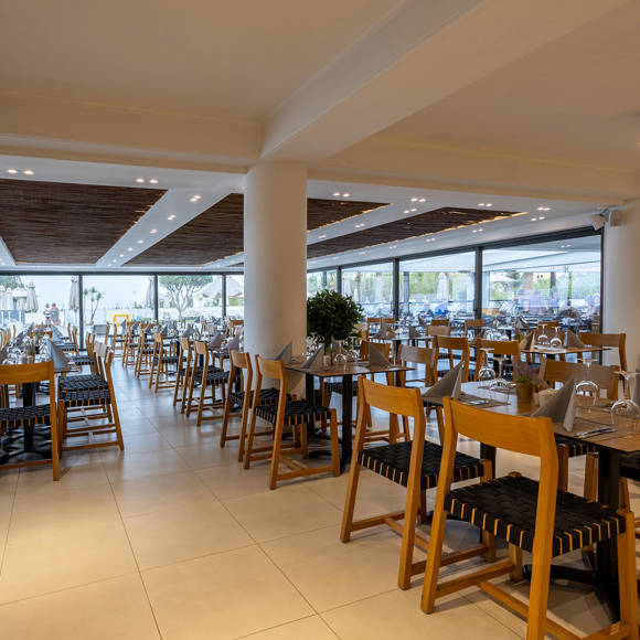 Spacious indoor restaurant with wooden ceiling, set tables and large windows overlooking the pool area
