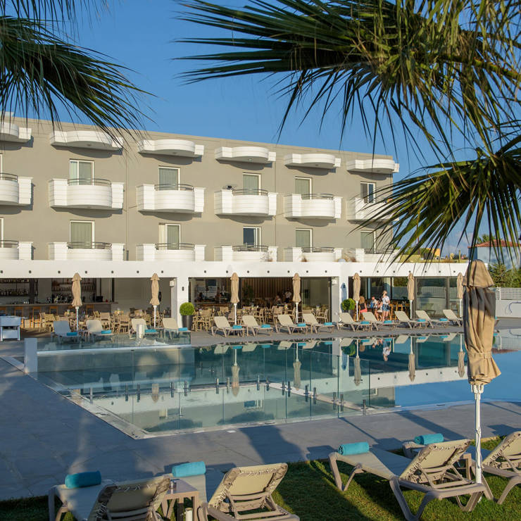 Dore hotel building with balconies, outdoor pool, sun loungers and palm trees in the foreground