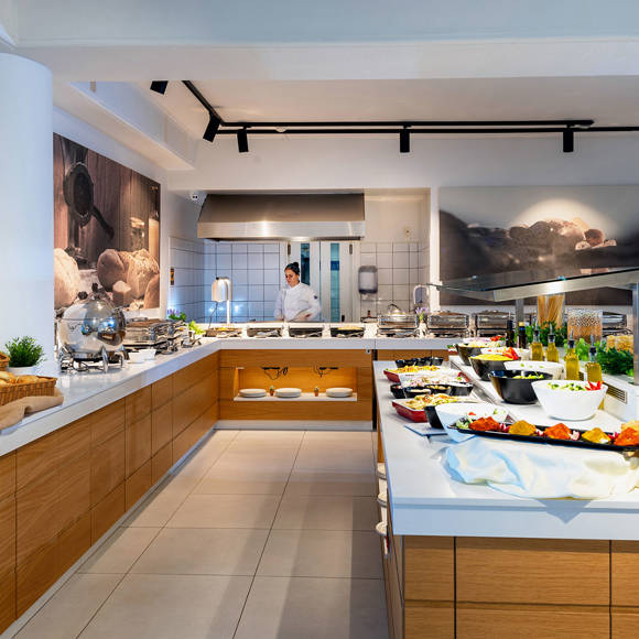 Buffet area with a wide selection of fresh dishes, bread baskets and a chef in the open kitchen
