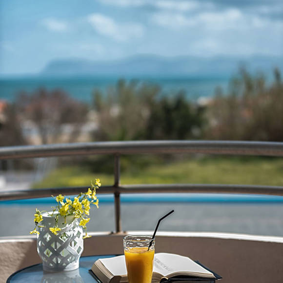 Balcony table with juice, book, and flower vase overlooking the sea