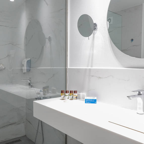 Modern bathroom with marble-style walls, large mirror, and minimalistic white sink with amenities