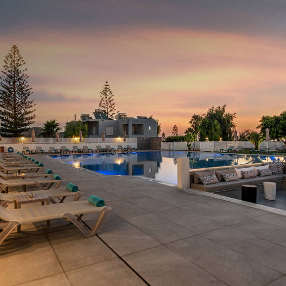 Poolside area at sunset with sun loungers, firepit seating and scenic lighting