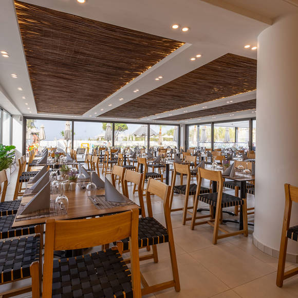 Spacious indoor restaurant with wooden ceiling, set tables and large windows overlooking the pool area