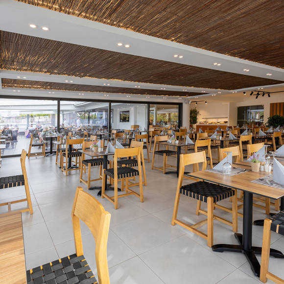 Modern restaurant with wooden chairs and tables, decorative ceiling panels and large windows