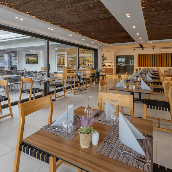 Spacious restaurant with wooden ceiling, set tables and large windows overlooking the pool area