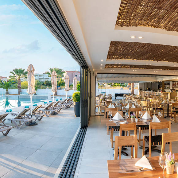Panoramic view of the hotel restaurant with open large windows leading to the pool area
