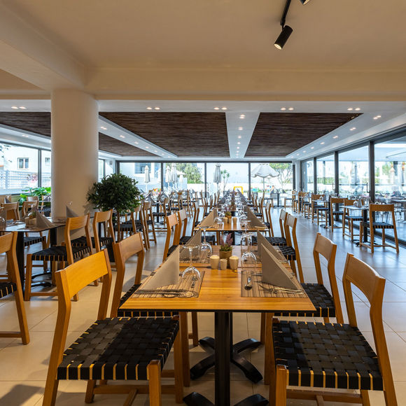 Spacious indoor restaurant with wooden ceiling, set tables and large windows overlooking the pool area