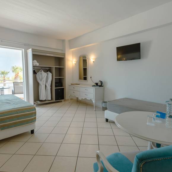 Quadruple room featuring a double bed, single beds, open wardrobe, vanity desk, and a balcony with sea view