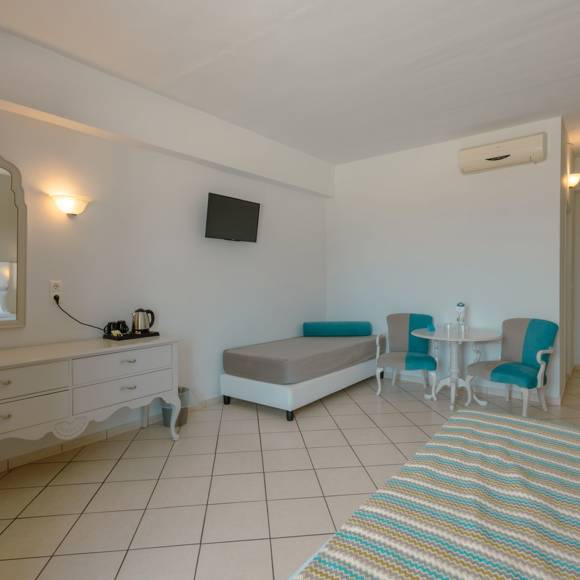 Quadruple room interior with two single beds, vanity desk, armchairs and a wall-mounted TV