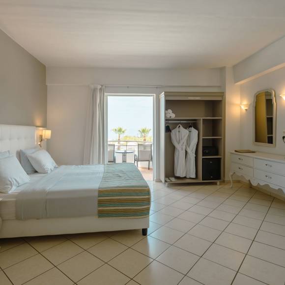 Quadruple room with a double bed, open wardrobe, vanity desk and balcony overlooking the sea
