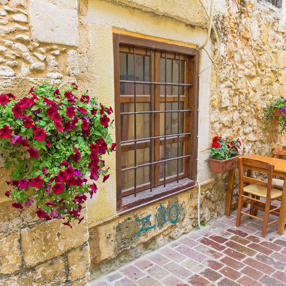 Traditional alley in Chania with stone walls, flowers and wooden tables