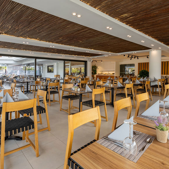 Modern indoor restaurant with wooden chairs and tables,  large windows and outdoor sitting area